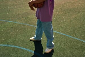 Person holding a basketball on an outdoor court in casual attire.