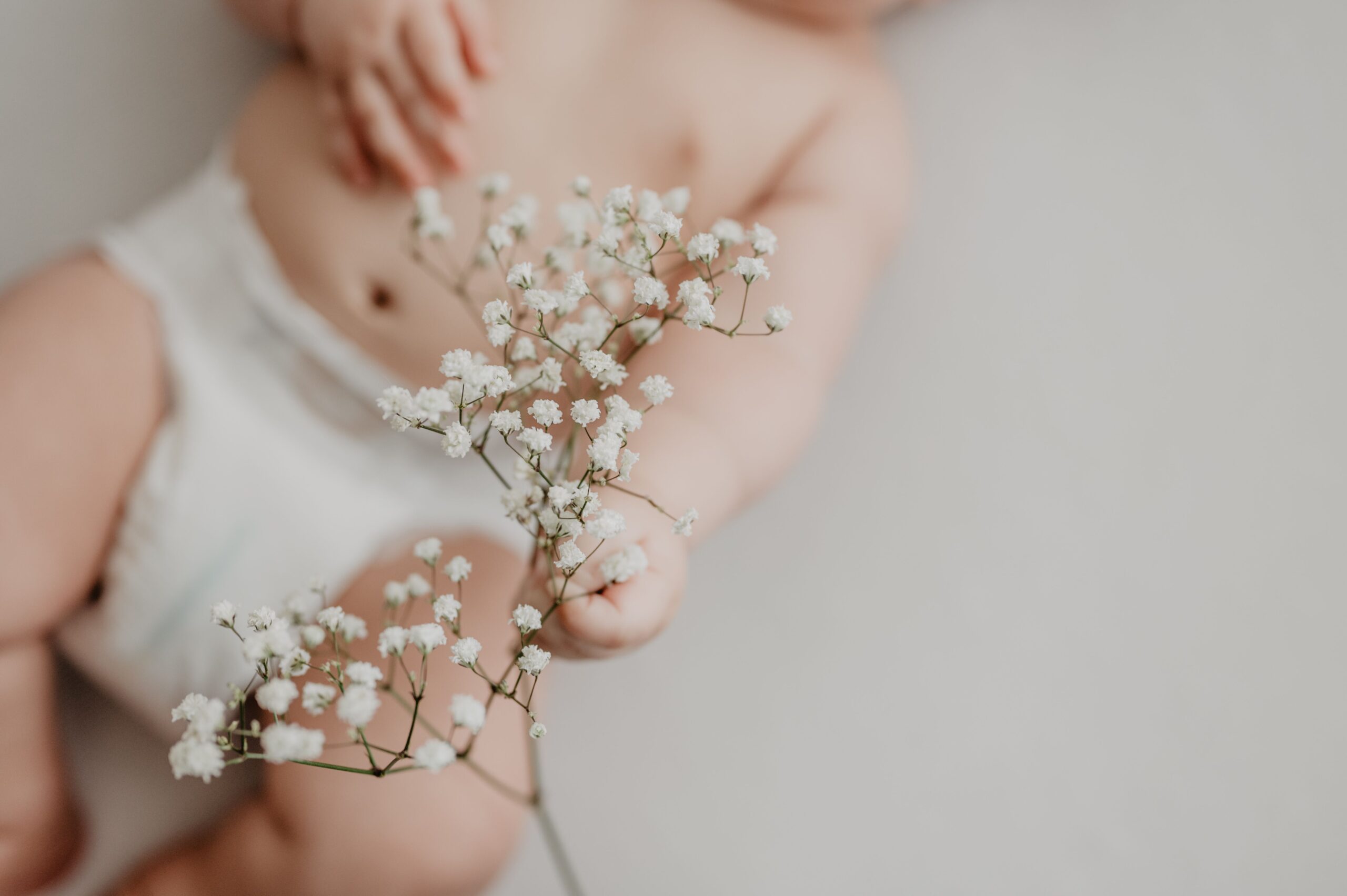 Contact Portrait of a baby in a diaper delicately holding white flowers, emphasizing innocence.