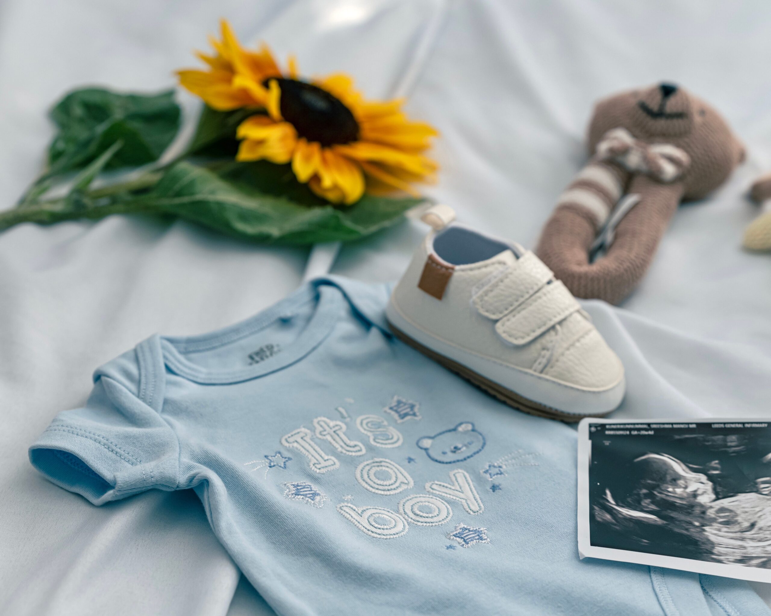 pexels photo 34191319 34191319 A charming baby announcement featuring a onesie, ultrasound, shoe, and sunflower on a soft blue background.