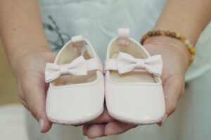 Adorable baby shoes with bows held in hands, perfect for a baby girl announcement or gift idea.