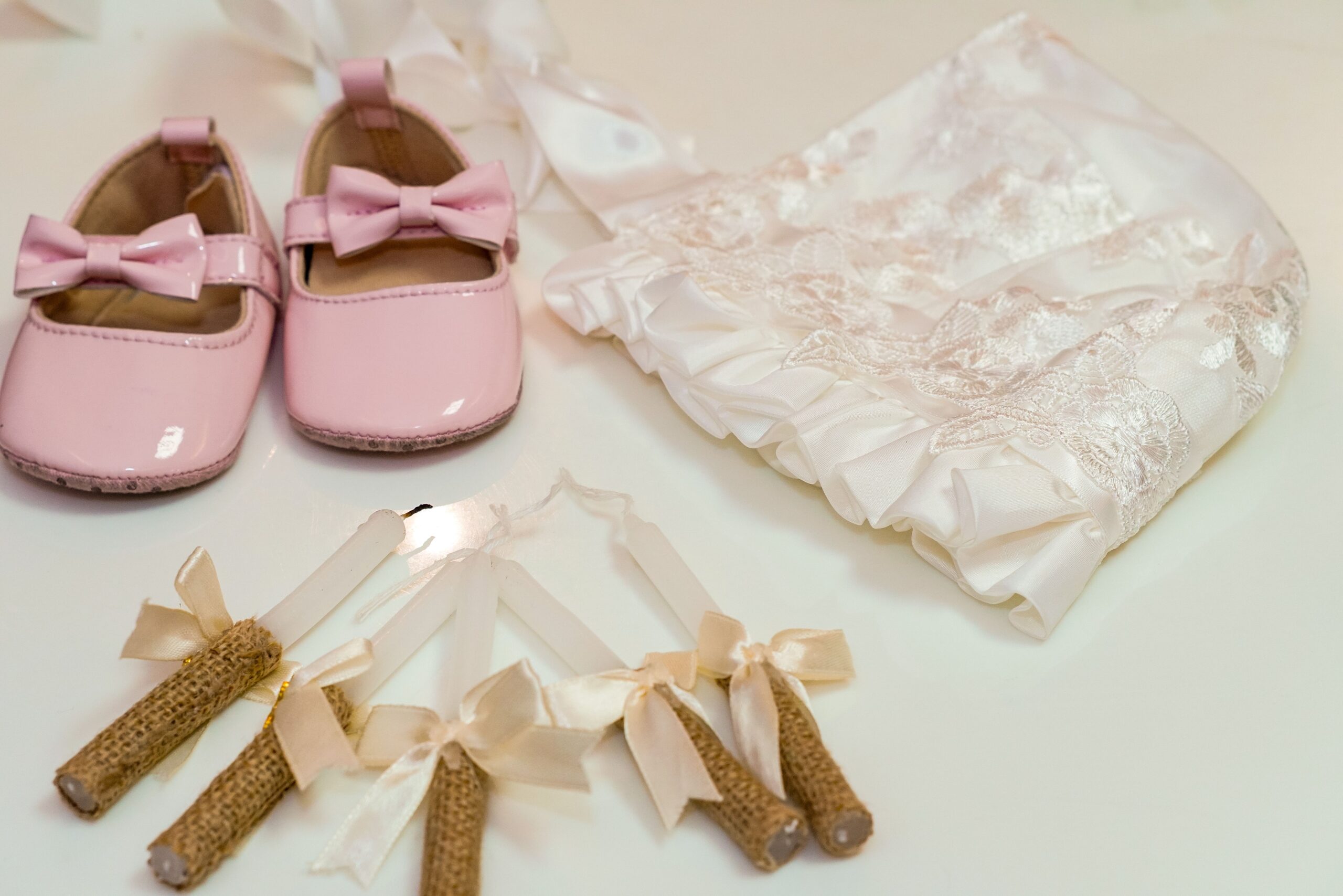 pexels photo 37621044 37621044 A collection of elegant baby christening accessories featuring pink shoes, a bonnet, and ribboned candles.