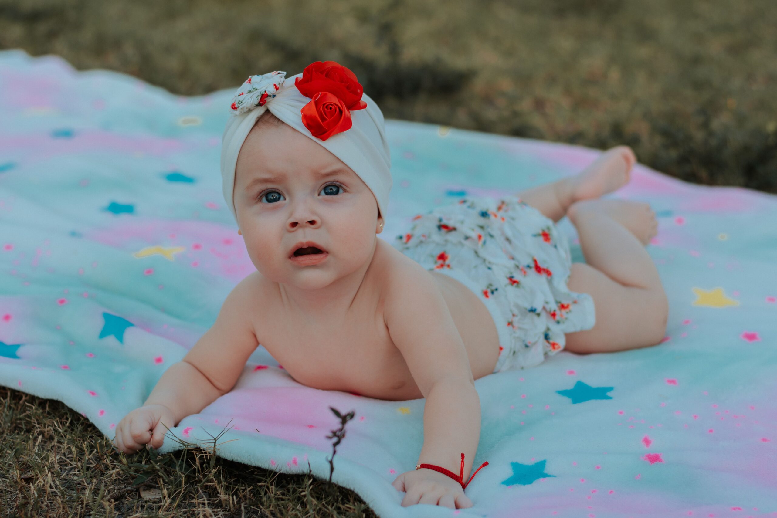 pexels photo 8773729 8773729 Adorable baby girl lying on a vibrant blanket outdoors with curious expression.