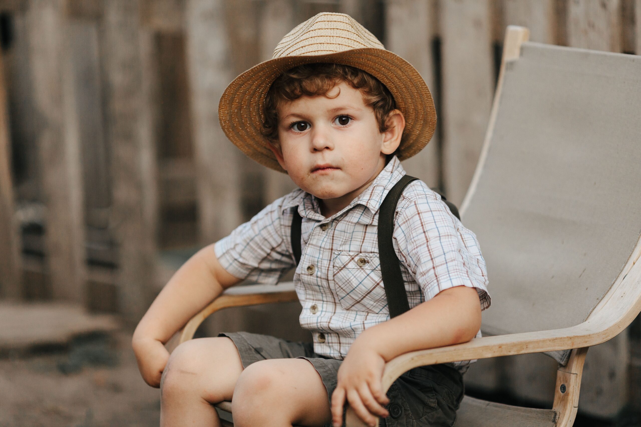 pexels photo 8836689 8836689 Adorable boy with straw hat seated on chair outdoors, exuding charm.
